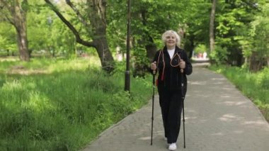 Aktif kıdemli yaşlı kadın parkta kayak direkleri ile İskandinav yürüyüşü eğitimi alıyor.