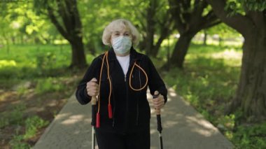 Karantinada parkta yürüyen, maske eğitimi alan kıdemli yaşlı kadın.