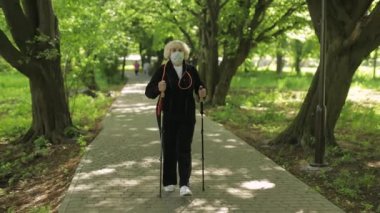 Karantinada parkta yürüyen, maske eğitimi alan kıdemli yaşlı kadın.