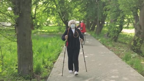 Aktivní starší žena v masce školení Nordic walking v parku v karanténě — Stock video