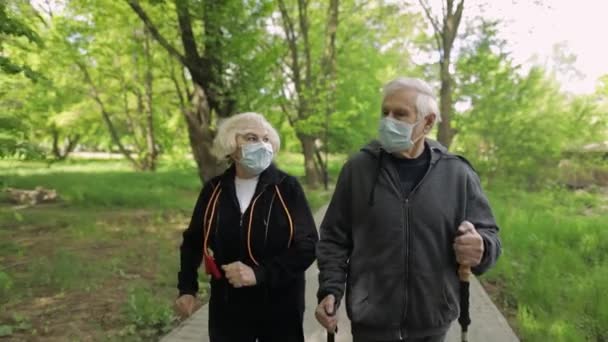 Actieve oudere man, vrouw die Nordic walking traint in het park tijdens quarantaine — Stockvideo