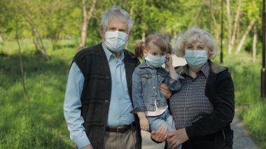 Tıbbi maskeli torunları olan yaşlı büyükanne ve büyükbabaları parkta yürürler. Coronavirüs