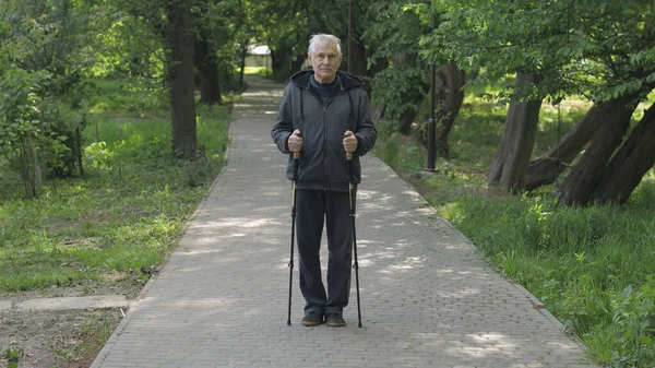 Aktivní starší muž trénink Nordic walking s lyžařskými trekkingovými tyčemi v parku — Stock fotografie