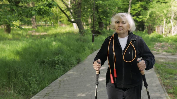 Vieille femme âgée active s'entraînant à la marche nordique avec des bâtons de ski de randonnée dans le parc — Photo