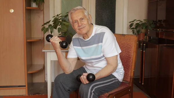Yaşlı, beyaz bir adam ağırlık kaldırıyor. Evde halter egzersizi yapıyor.