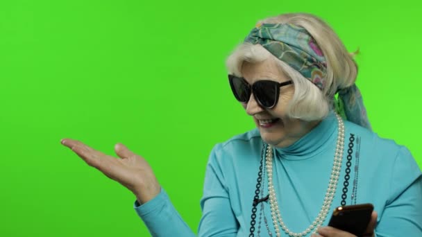 Mulher avó branca usando smartphone, apontando para algo com a mão — Vídeo de Stock