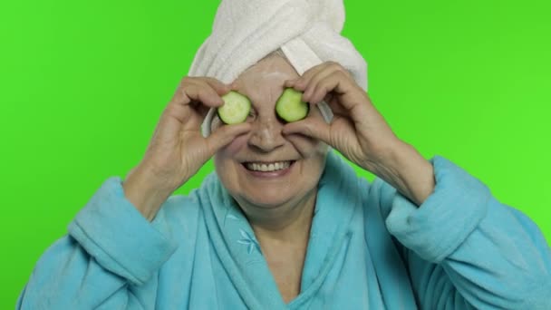 Oudere oma in badjas na de douche. Oude vrouw met plakjes komkommer — Stockvideo