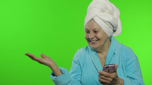 Ηλικιωμένη γιαγιά με μπουρνούζι. Γριά γυναίκα με smartphone να δείχνει κάτι. — Αρχείο Βίντεο