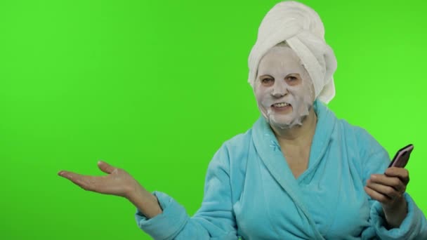 バスローブ、フェイスマスクの祖母。スマートフォンを指差している女性 — ストック動画