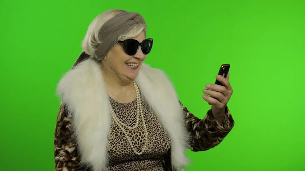 La nonna caucasica anziana usa lo smartphone per parlare di videochiamate. Chiave cromatica — Foto Stock