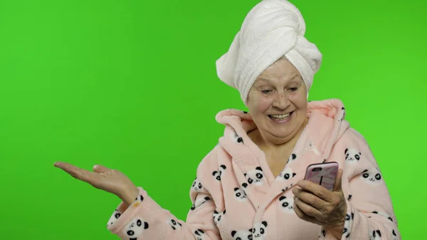 Abuela anciana en albornoz. Anciana con smartphone apuntando a algo —  Fotos de Stock