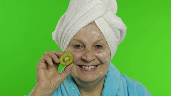 Elderly grandmother in bathrobe. Old woman with half of kiwi in her hand — Stock Photo, Image
