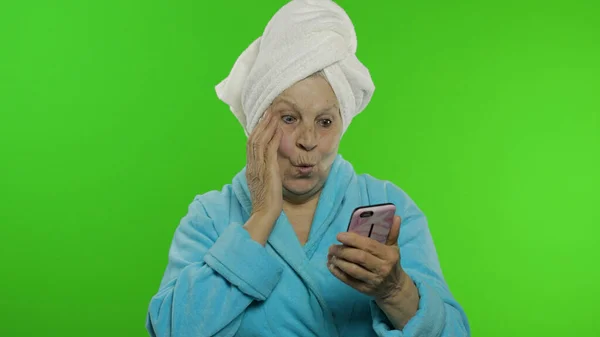 Idős nagymama zuhanyzás után. Az idős nő okostelefont használ az online vásárláshoz — Stock Fotó