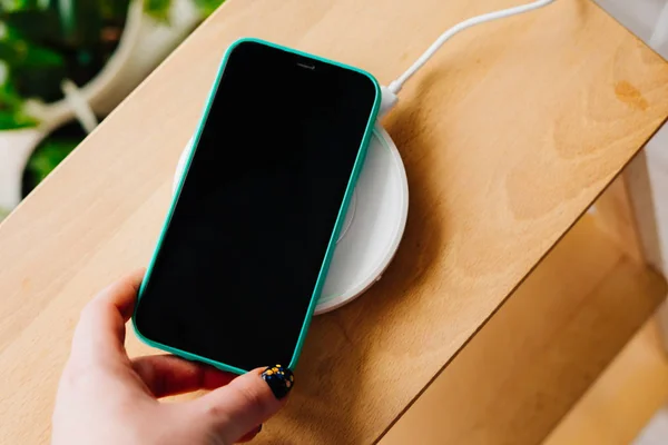 Smartphone in mint silicone case is charged from a wireless charger.