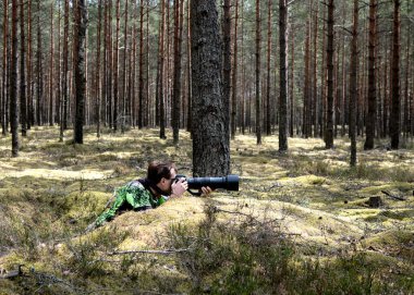 Adam fotoğrafçı ormanda saklanıyor ve vahşi hayvanların fotoğraflarını çekmeye hazırlanıyor.