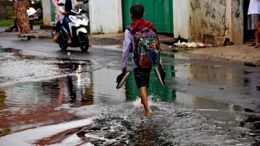  24 Şubat 2020, Pekalongan, hala yağmurlu koşullarda sel basmış yollardan geçen vatandaşlar ve okul çocukları