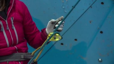 Spor salonundaki duvarın önünde bir kişi duruyor ve duvara tırmanan kişiye daha fazla ip veriyor..