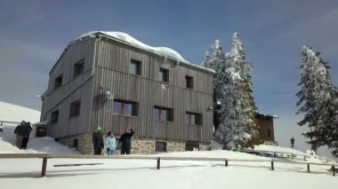 Büyük siyah dağ kulübesinin önünde duran birkaç yürüyüşçü var ve temiz havanın tadını çıkarıyorlar..