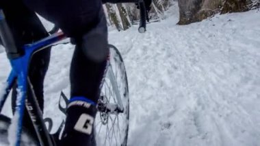 Bir adam, donmuş nehrin yanındaki karlı ve kaygan yollarda bisikletini sürerken doğayı gözlemliyor..