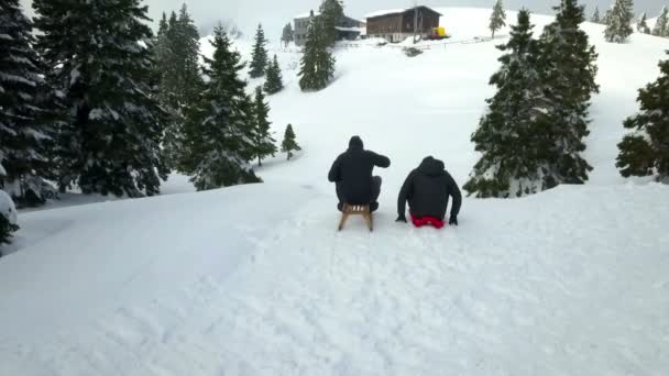 两个人坐在山顶上的雪橇上 他们给了每一个高五和雪橇下山 风景美丽 白雪连绵 — 图库视频影像