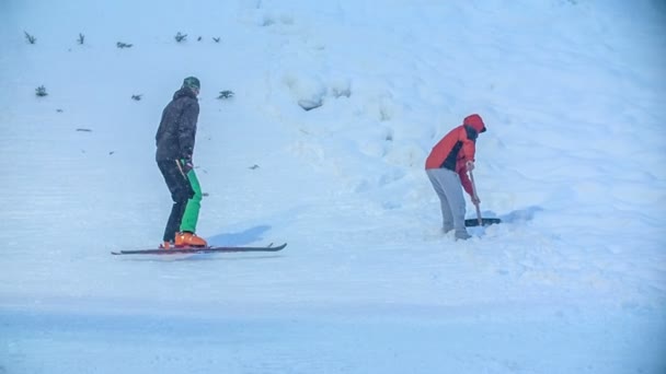 若いスキージャンパーがジャンプして練習できるように 2人の男性が一定の雪のためにトラックを固定しています — ストック動画