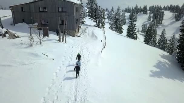 三个人走在雪地上狭窄的小径上 远离山间小屋 空中射击 — 图库视频影像