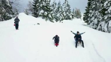 Tepeden en hızlı kızakla inecek üç kişi yarışacak. Mutlu ve neşeli görünüyorlar. Hava görüntüsü. Dağlarda kış mevsimindeyiz. Dışarıda biraz zaman geçiriyorlar..