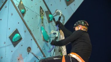 Genç bir dağcı dikkatlice duvara tırmanıyor ve duvar panelleri için kendini tutuyor..