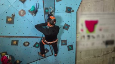 Bir adam spor salonunda tırmanma pratiği yapıyor. Çok dikkatli görünüyor..