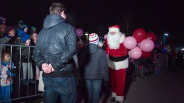 Noel Baba cömertçe onu Noel pazarında karşılamaya gelen çocuklara kırmızı ve pembe balonlar veriyor..