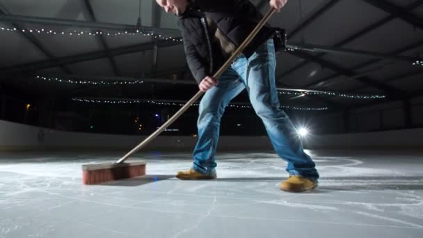 一个男人站在冰上 用扫帚清扫冰 在冰上很滑 — 图库视频影像