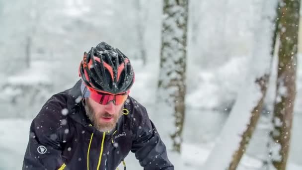 スポーツマンは冬の時間にサイクリングしている 彼はヘルメットをかぶっている 雪が降っている — ストック動画