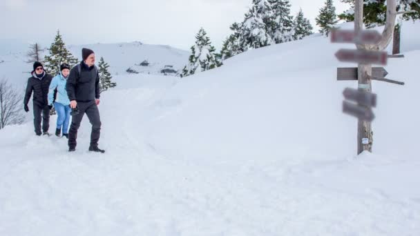 丘のどこかの雪の中に立っている看板には3人が来ています 冬の時間だ — ストック動画