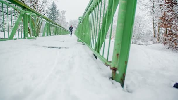 スポーツマンは雪で覆われた橋を渡ってサイクリングしている 冬だし朝早く外に出てるのは彼だけみたい — ストック動画