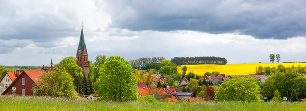 Gietrzwad - Polonya 'nın Warmia ve Mazury kentlerinde bir köy - bahar manzarası, çiçek açan kolza tohumu. Gietrzwad 'daki Kutsal Bakire Meryem' in Doğumu Bazilikası.