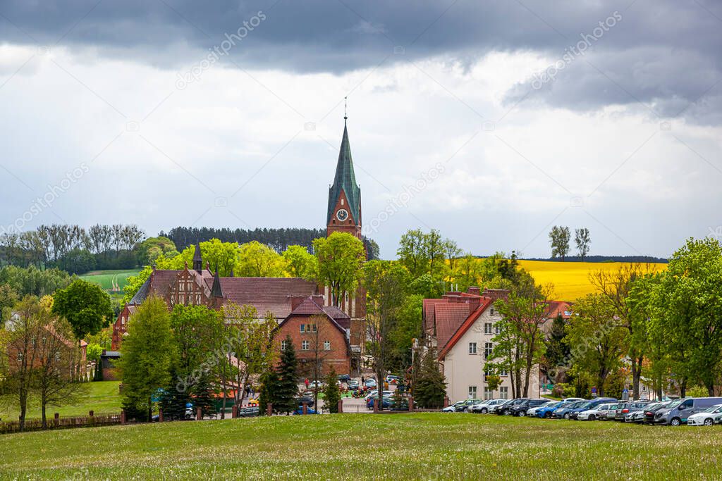 Gietrzwad - a village in Warmia and Mazury, Poland - spring landscape, blooming rapeseed. Basilica of the Nativity of the Blessed Virgin Mary in Gietrzwad.