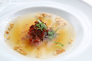 Kurutulmuş domates ve kavrulmuş çam fıstığı eklenmiş şeffaf domates çorbası..