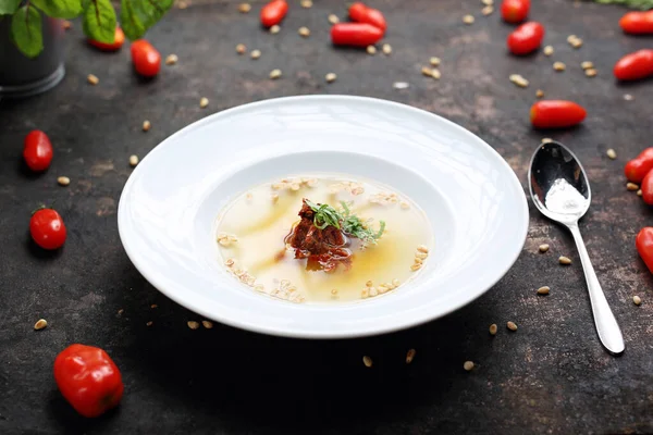 Consome, aromatische transparante tomatensoep met toevoeging van gedroogde tomaten en geroosterde pijnboompitten. — Stockfoto