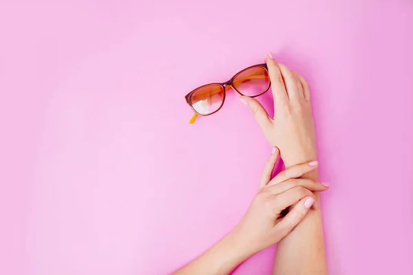 Weibliche Hände mit Brille auf rosa Hintergrund. — Stockfoto