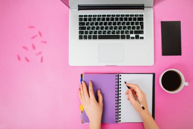 Kadın eli, dizüstü bilgisayarı ve dizüstü bilgisayarı olan düz yatak. Pembe masa.