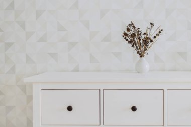 Interior with dried flowers in a white vase on the empty wall background.