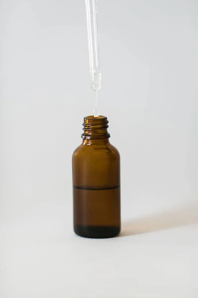 Cosmetic pipette and dark oil bottle with drop closeup on white background.