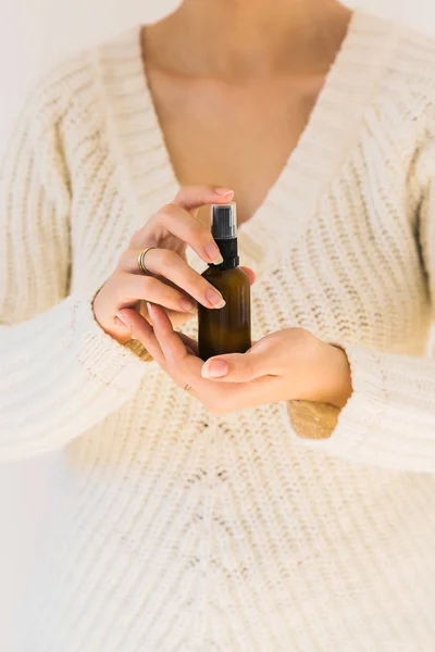 Woman holding a bottle with natural skincare product.