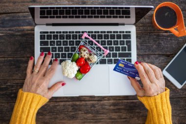 Yaşlı bir kadın kredi kartıyla online alışveriş yapıyor. Özellikle Coronavirus 'tan sonra alışveriş arabasıyla ticaret konsepti.