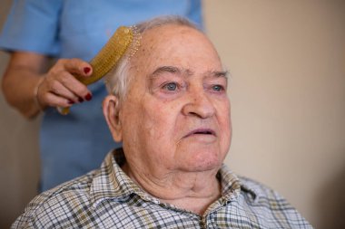 Hemşire, yaşlı bir adamın saçını tarıyor taraklı, evde bakım konseptiyle bir hemşireyle.