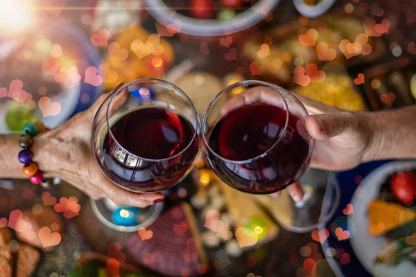Restoranların masasında kadeh kaldıran kırmızı şarap kadehleriyle kutlama yapan bir çiftin yakın çekimleri. Sevgililer Günü için kalp şeklinde sahte efektler içeren tezahürat konsepti