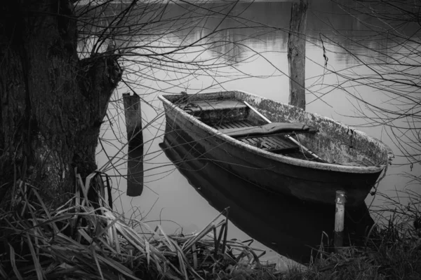 Um barco a remo abandonado está ancorado na margem de um lago e — Fotografia de Stock