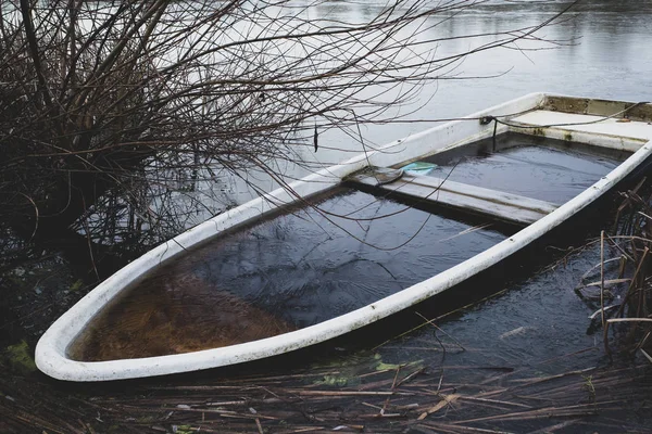 Um barco a remo afundado fica na margem de um pequeno lago congelado — Fotografia de Stock