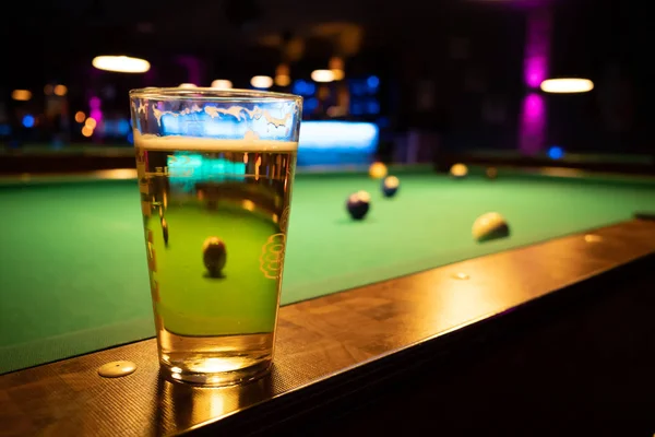 In a billiard parlor on the rail of a pool table is a glass with — 스톡 사진