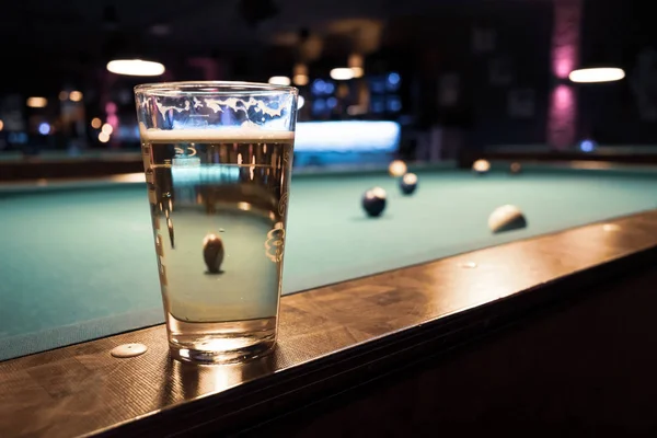 In a billiard parlor on the rail of a pool table is a glass with — 스톡 사진